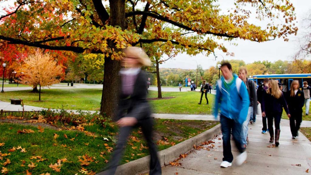 People walking in a park during autumn with colorful trees and a blue bus in the background.