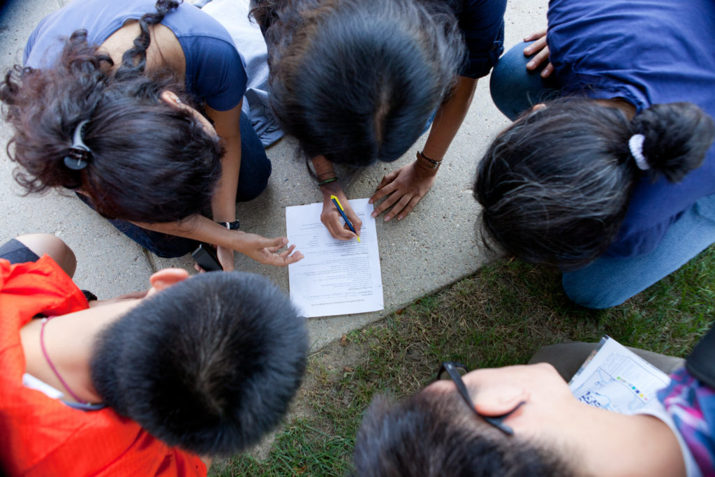 students in a group with their heads down facing a collaborative worksheet