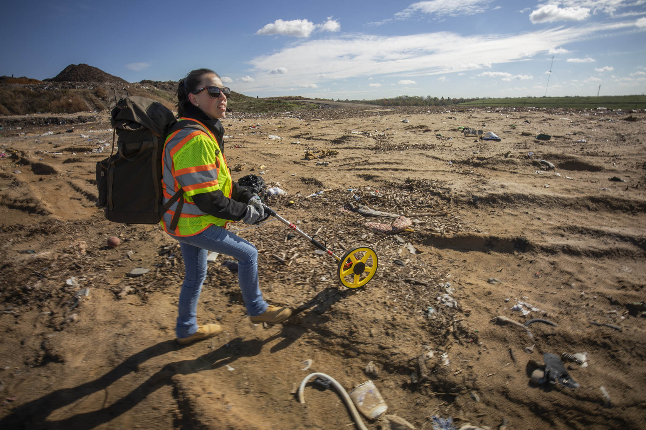 woman pushing a wheeled measurement device across a landfill