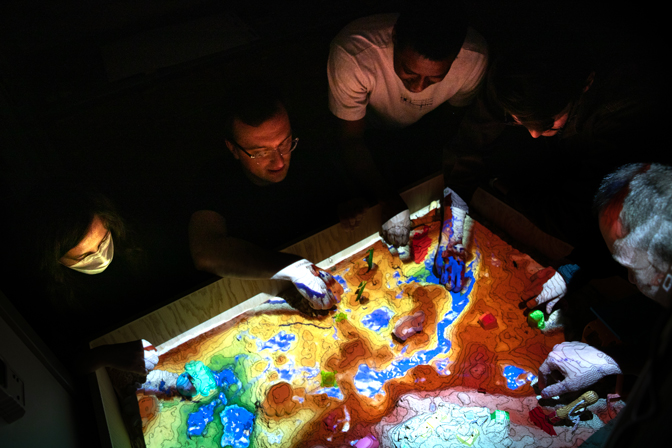 Kerkez with an Augmented Reality Sandbox in his lab. The sandbox allows users to digitally change the physical topography and hydrology of the space to better understand interactions to changes in the environment.