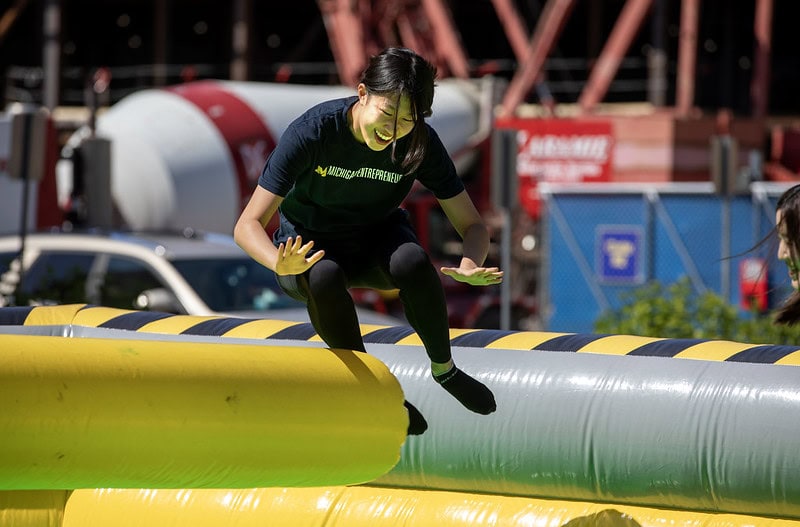 A student laughs while leaping over an inflatable beam