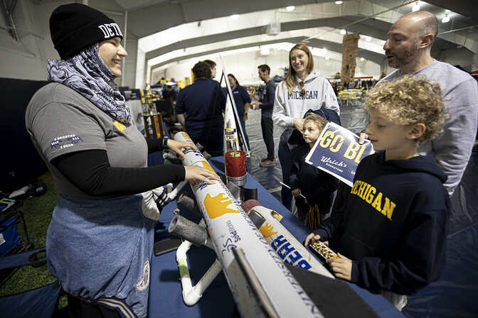 Group of people interacting in an indoor tailgate setting with a model or display piece.