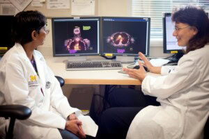Two researchers in lab coats working at a desktop computer, reviewing the monitor