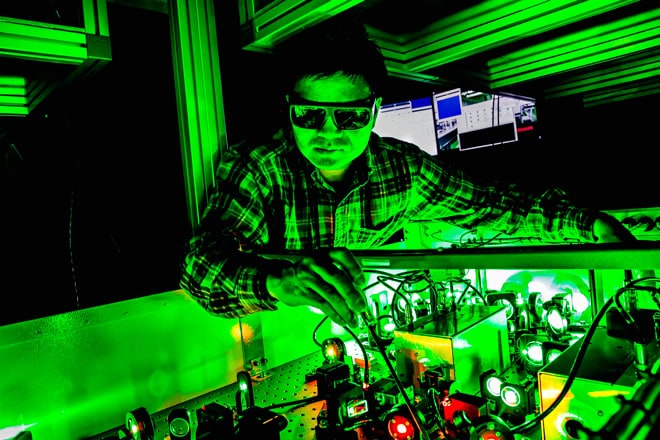 A person adjusts a piece of lab equipment. The room is dark but illuminated by a vibrant green light.