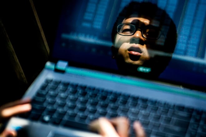 Reflection of a person on a laptop screen with visible keyboard and blurred text.