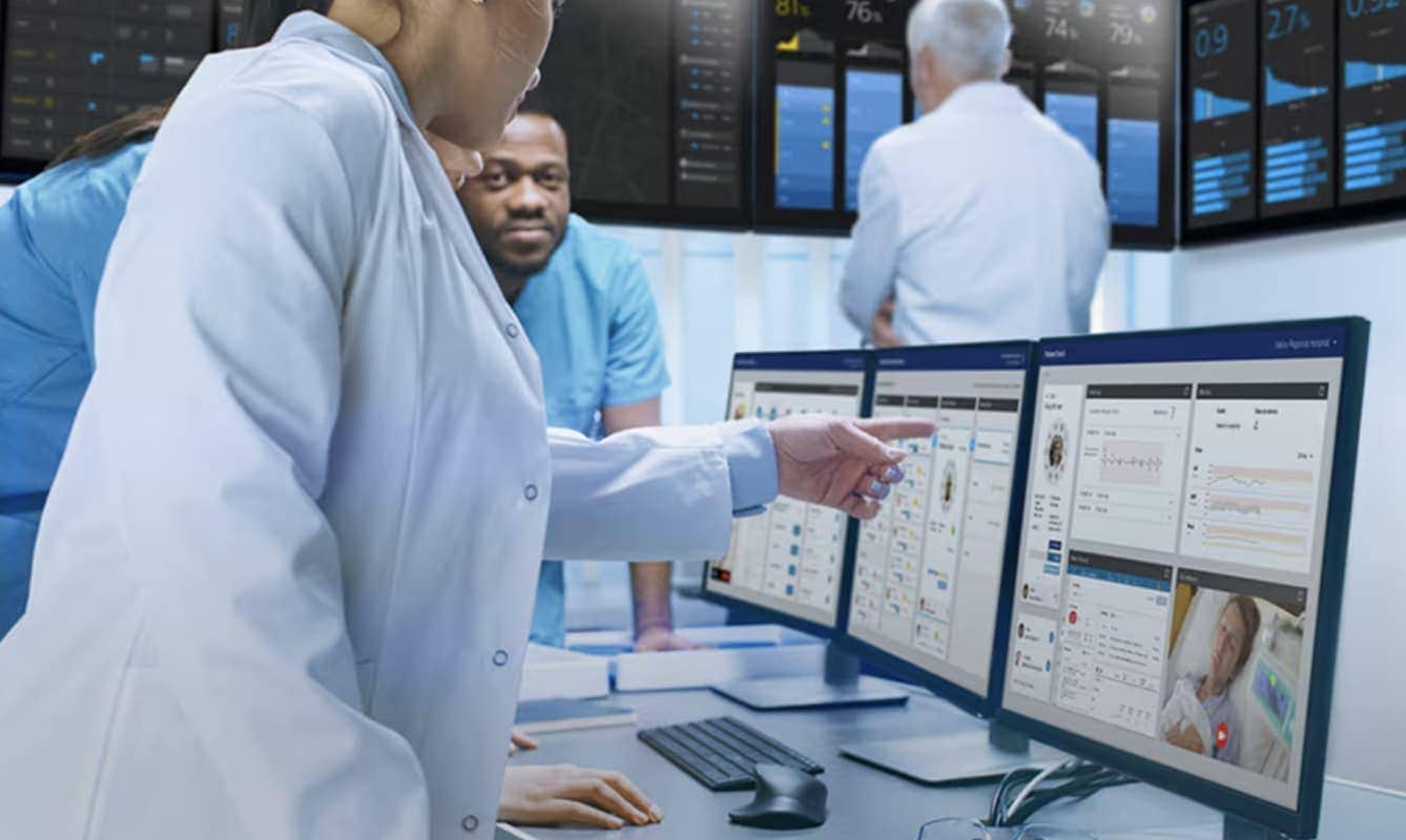 Workers in lab coats examine and discuss results on a screen.