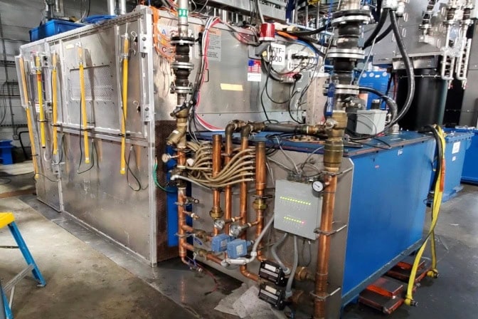 Industrial equipment featuring metallic structures, yellow hoses, copper pipes, blue box, and control panel with cables.