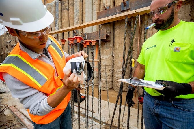 Two construction workers at a building site examining a device on a building site.