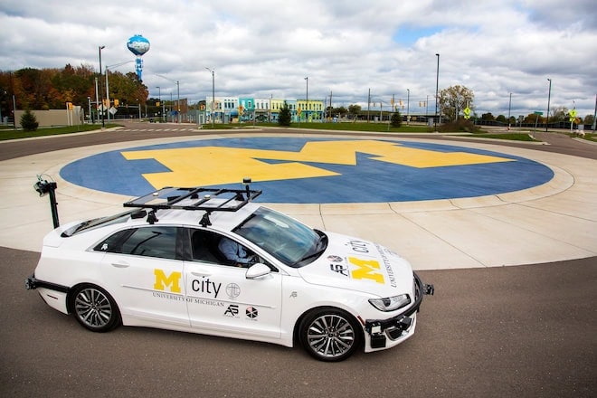 An Mcity vehicle with sensors around the frame of the car idles in a roundabout inside Mcity.