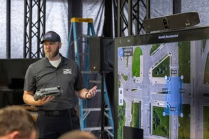 An instructor stands in front of a screen holding a drone remote controller