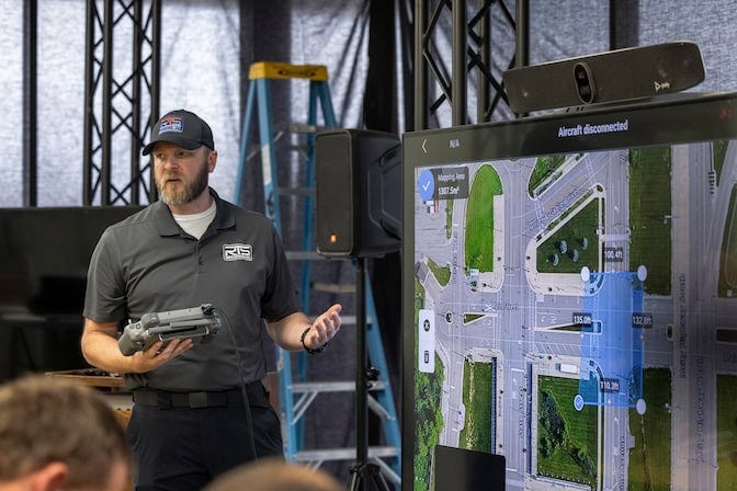 An instructor stands in front of a screen holding a drone remote controller