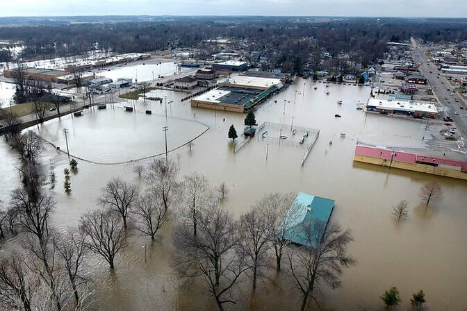 Aerial view of a flooded town with submerged roads, fields, and buildings.