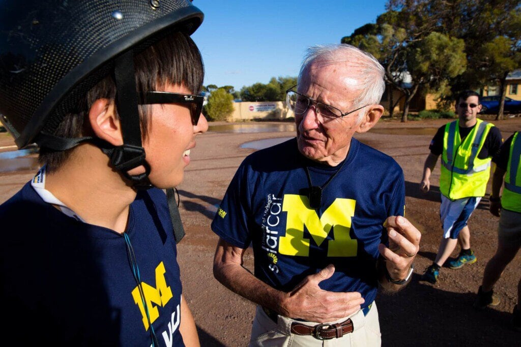 A man is in conversation with a student. Both are wearing blue Michigan solar car T-shirts.