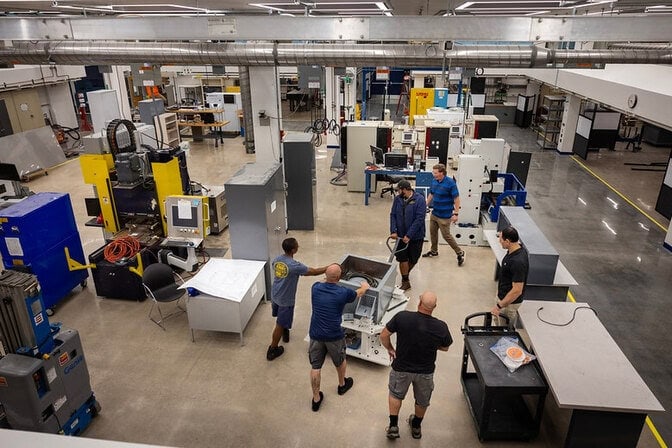 The DOW manufacturing space, which features a warehouse with machinery and six people gathered around a table.