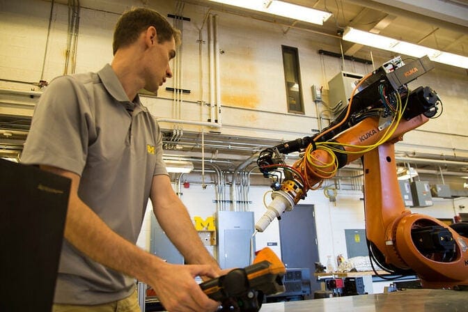 A man operates a KUKA robotic arm in a workshop.