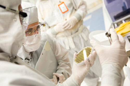 Individuals in cleanroom suits examining a circular piece of equipment in a lab setting.