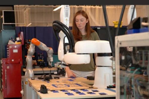 A woman in a lab with robotic arms and components on a table.