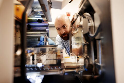 A person wearing blue rubber gloves inspecting lab equipment in a technical setting.