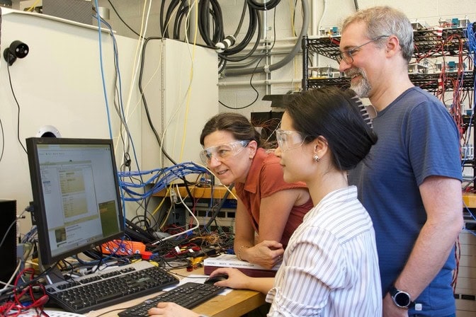 Three researchers look at a monitor in a research lab