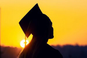 A silouhette of a student in a cap and gown at sunset