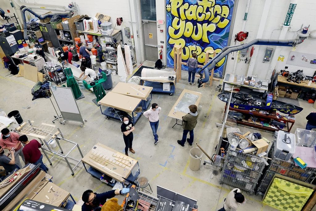 Image of the inside of a active lab space with various equipment and supplies. Students are in the process of talking, working, and interacting with equipment.